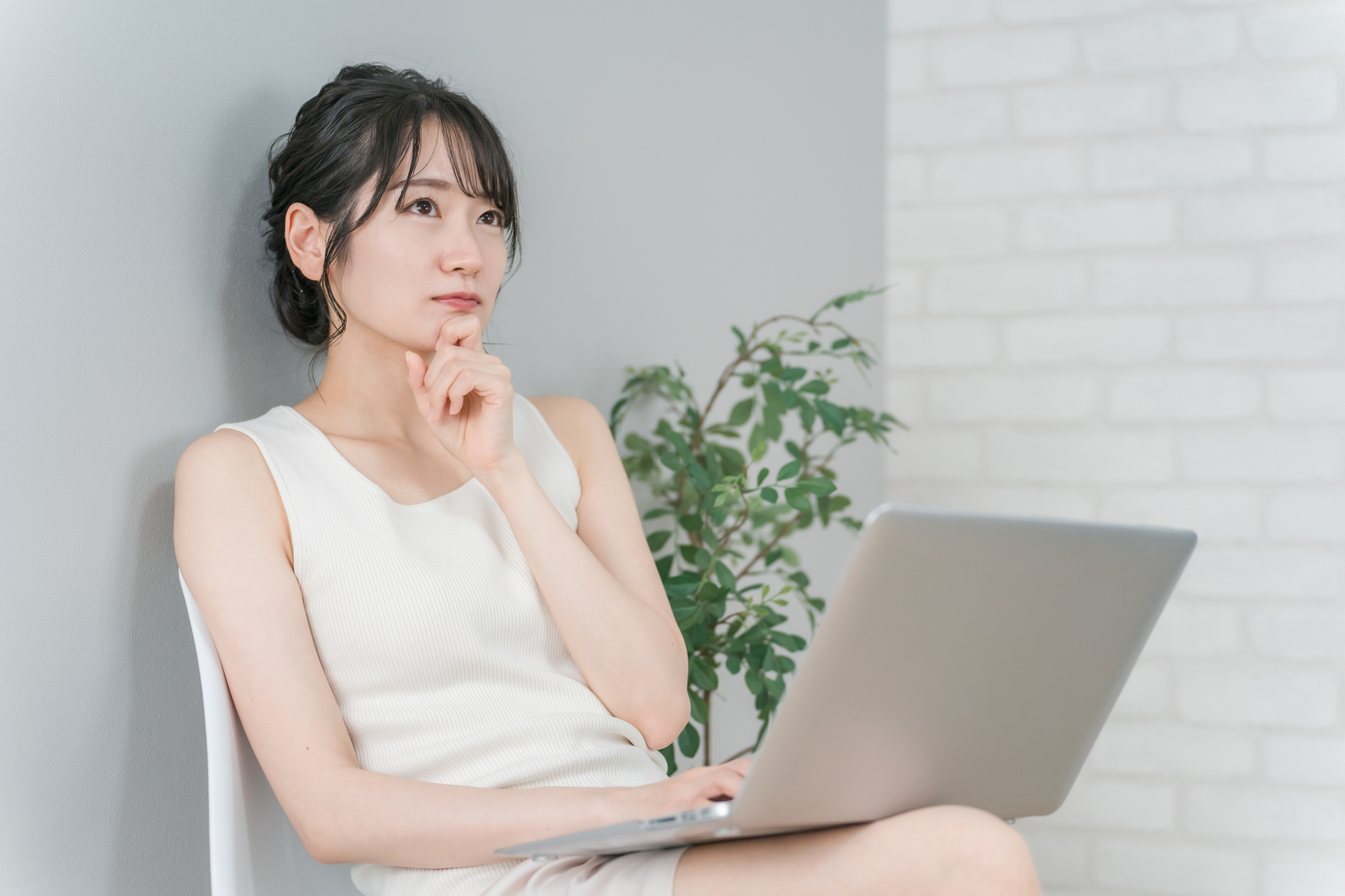 自宅のデスクでPCに向かい、手が止まって悩んでいる30代の女性